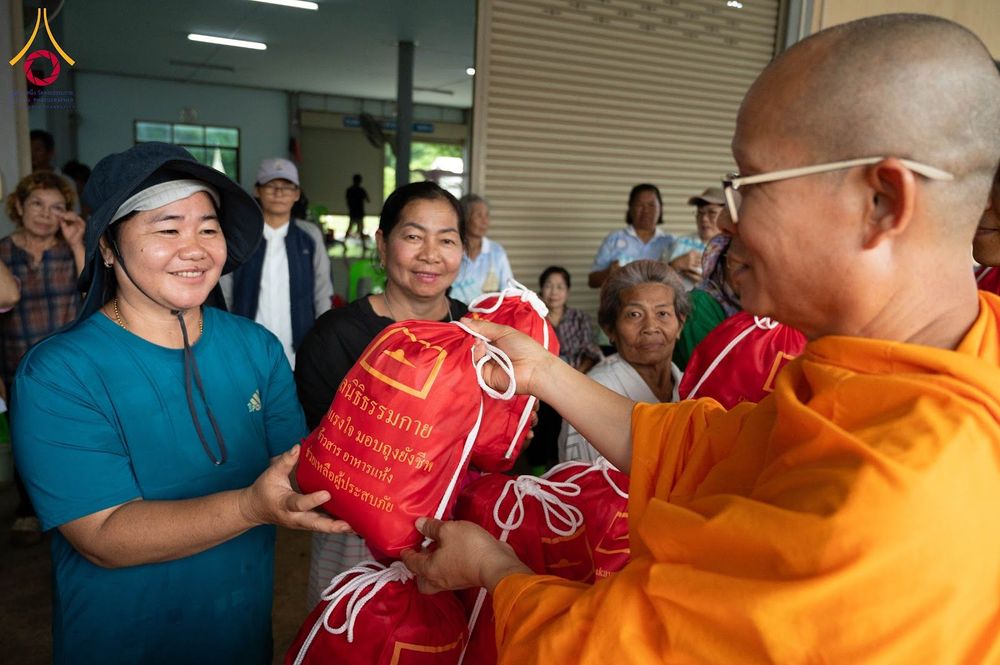 พระสงฆ์กำลังส่งมอบถุงยังชีพสีแดงให้แก่หญิงไทยท่ามกลางกลุ่มชาวบ้านที่มารับความช่วยเหลือ