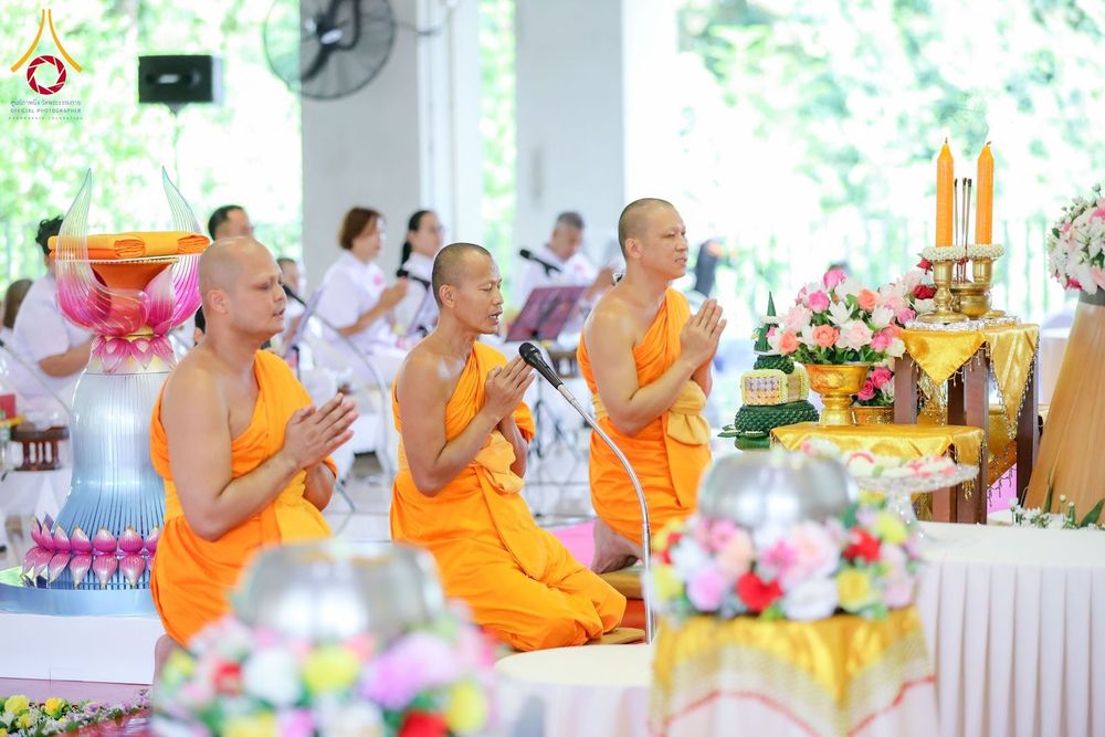 พระสงฆ์ 3 รูปนั่งพนมมือประกอบพิธีกรรมทางศาสนาภายในอาคารที่มีผู้เข้าร่วมโครงการสวมชุดสีขาว