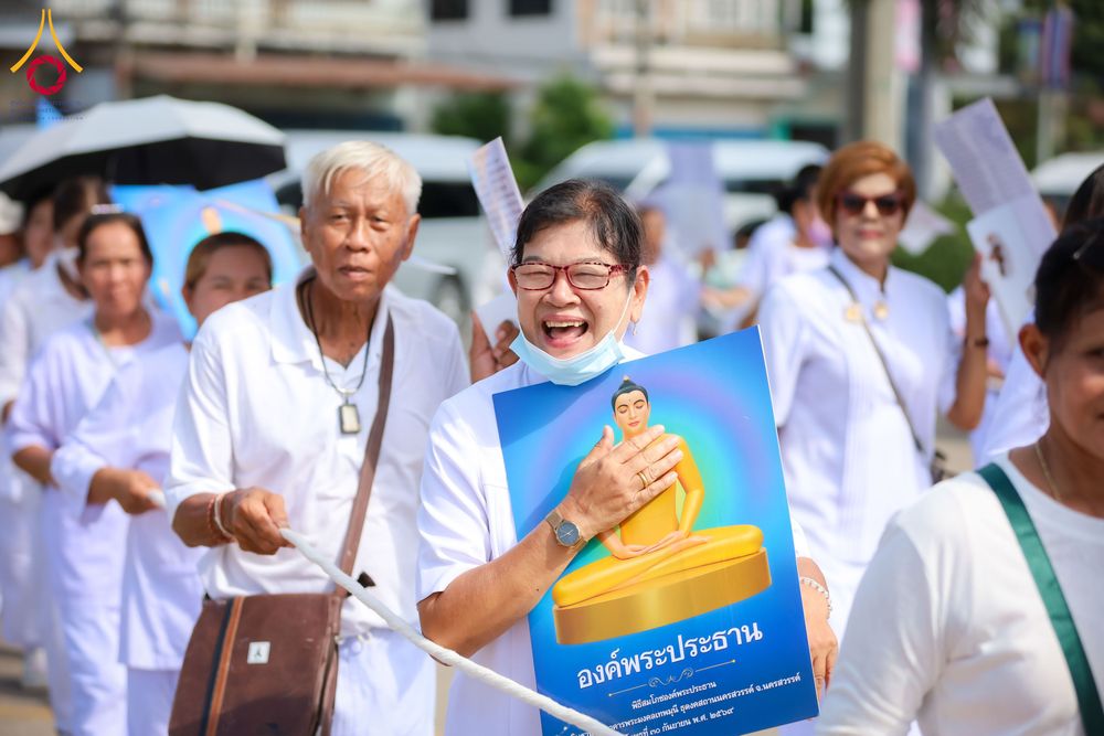 กลุ่มคนสวมชุดขาวถือป้ายภาพพระประธานเดินในขบวนกลางแจ้ง