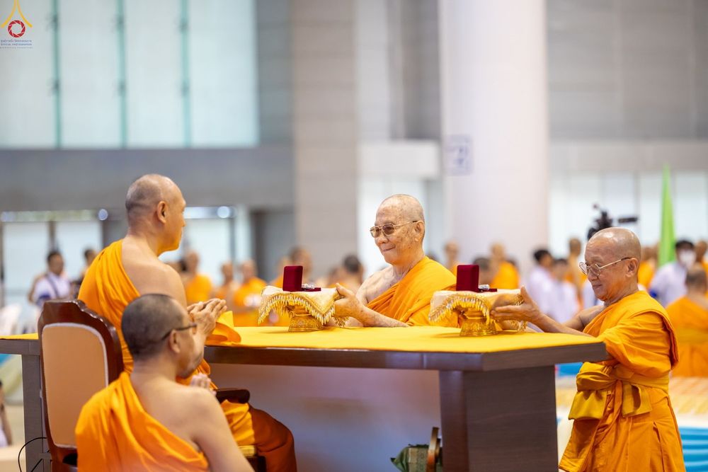 พระภิกษุสงฆ์ในจีวรสีส้มกำลังทำพิธีมอบพระของขวัญบนโต๊ะที่มีผ้าคลุมสีเหลือง