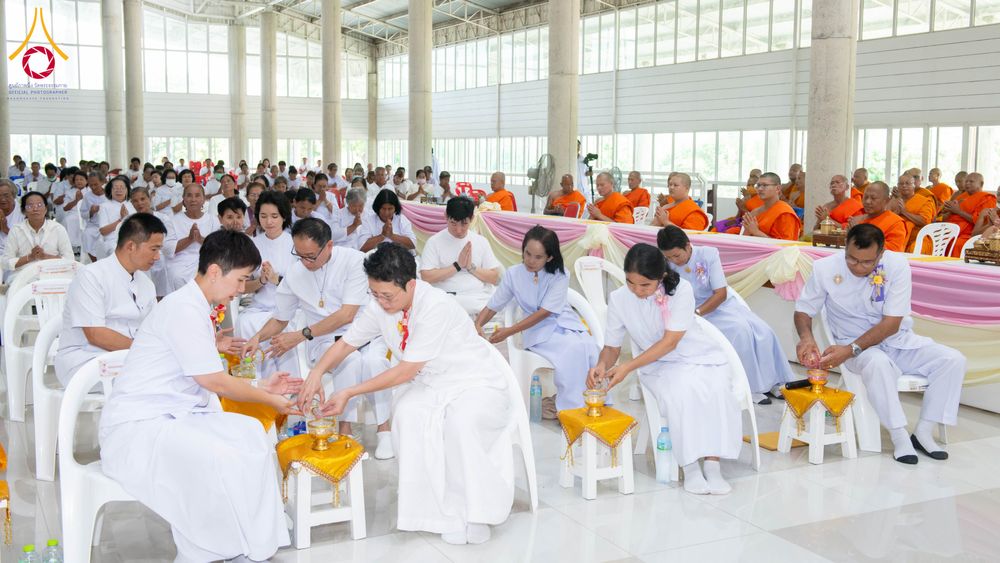 กลุ่มพุทธศาสนิกชนในชุดสีขาวกำลังประกอบพิธีกรรมทางศาสนาภายในอาคารโถงกว้าง