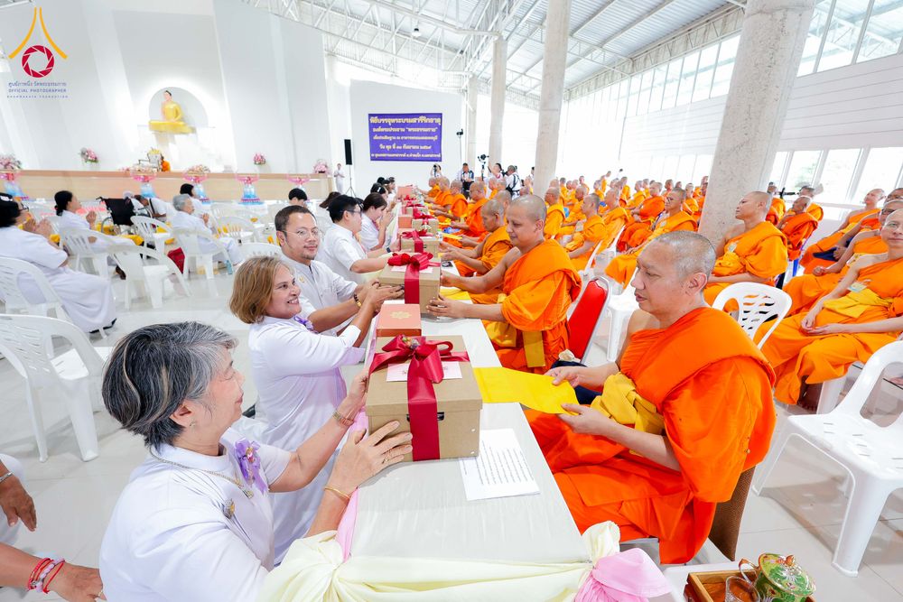พุทธศาสนิกชนในชุดขาวกำลังถวายกล่องของขวัญและปัจจัยแด่พระภิกษุสงฆ์ในพิธีทางศาสนา