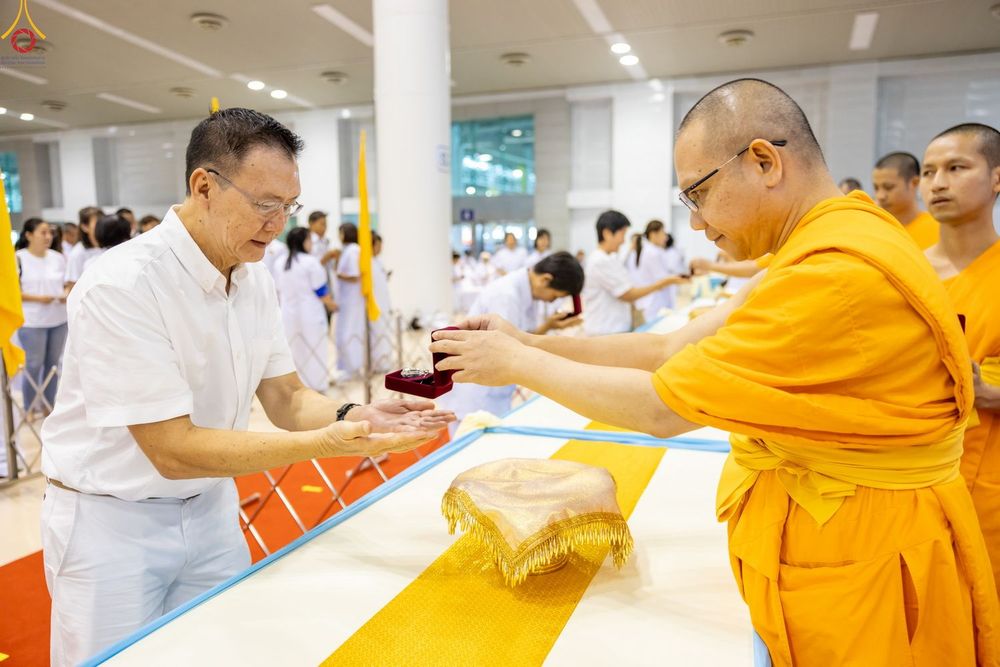 พระภิกษุสงฆ์มอบพระของขวัญให้แก่ชายในชุดสีขาวภายในห้องโถง