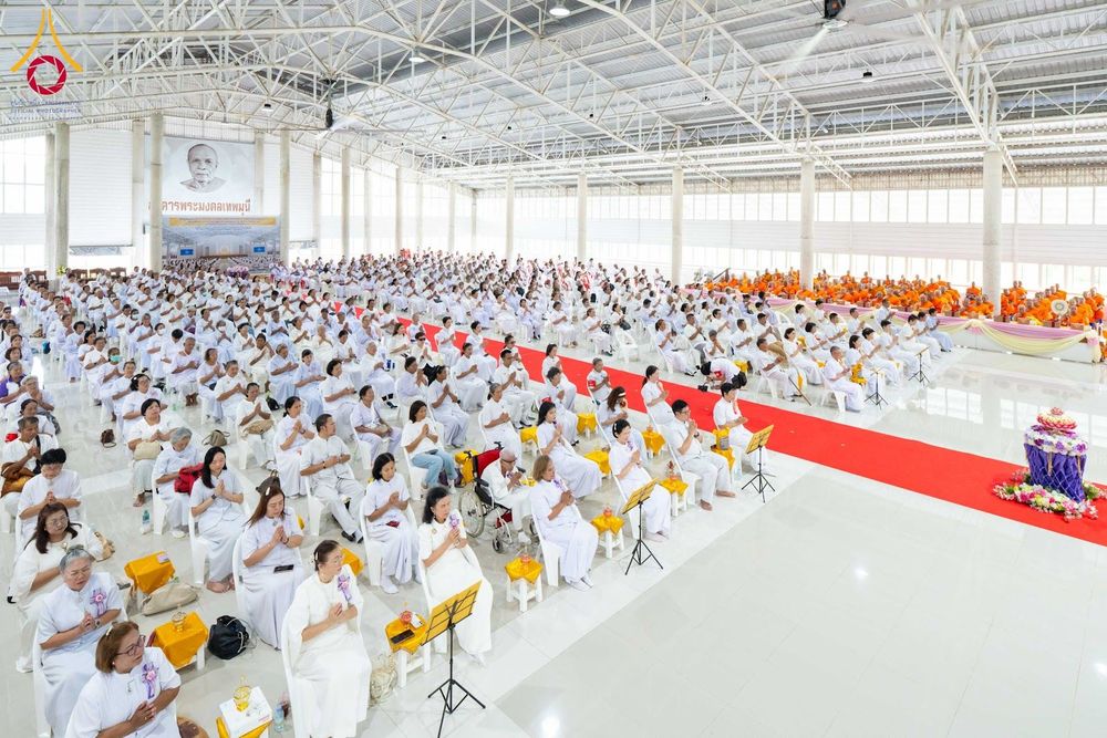 กลุ่มพุทธศาสนิกชนชุดขาวนั่งร่วมพิธีทางศาสนาภายในอาคารกว้างขวาง