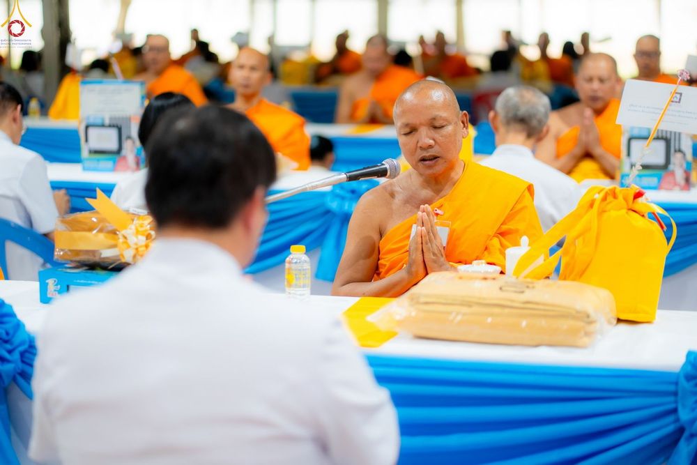 พระสงฆ์กำลังประนมมือพูดผ่านไมโครโฟนในงานพิธีทางศาสนาที่มีคณะสงฆ์และฆราวาสเข้าร่วม
