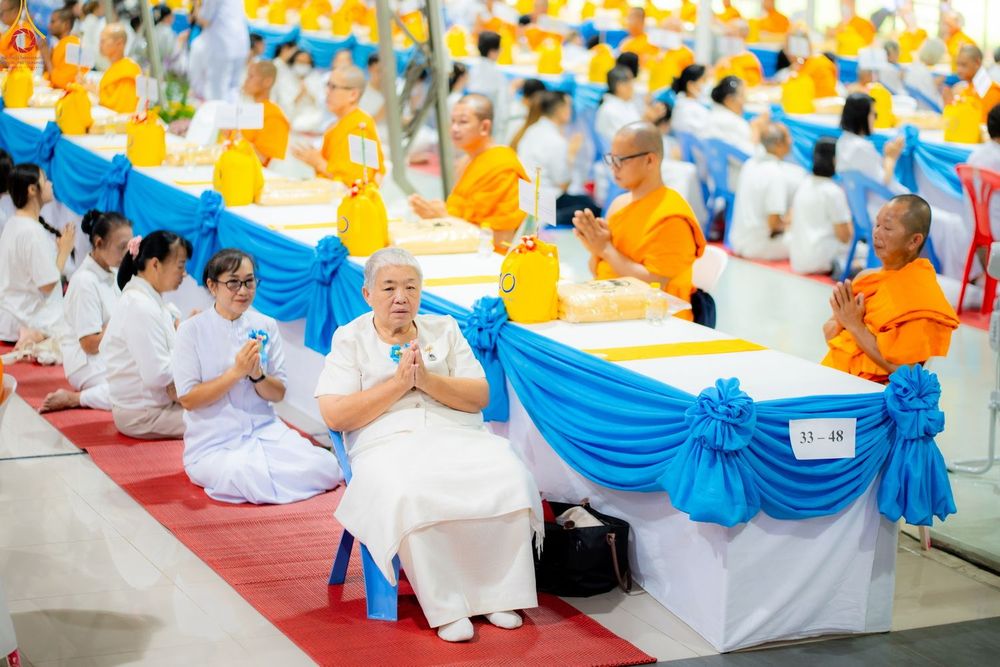 กลุ่มพุทธศาสนิกชนสวมชุดขาวและพระภิกษุสงฆ์นั่งพนมมือร่วมพิธีทางศาสนาภายในอาคาร