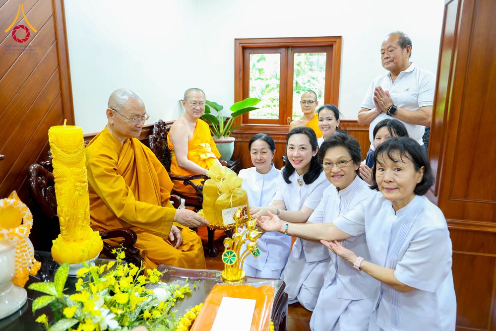 กลุ่มพุทธศาสนิกชนในชุดสีขาวกำลังถวายเทียนพรรษาและเครื่องไทยธรรมแด่พระสงฆ์