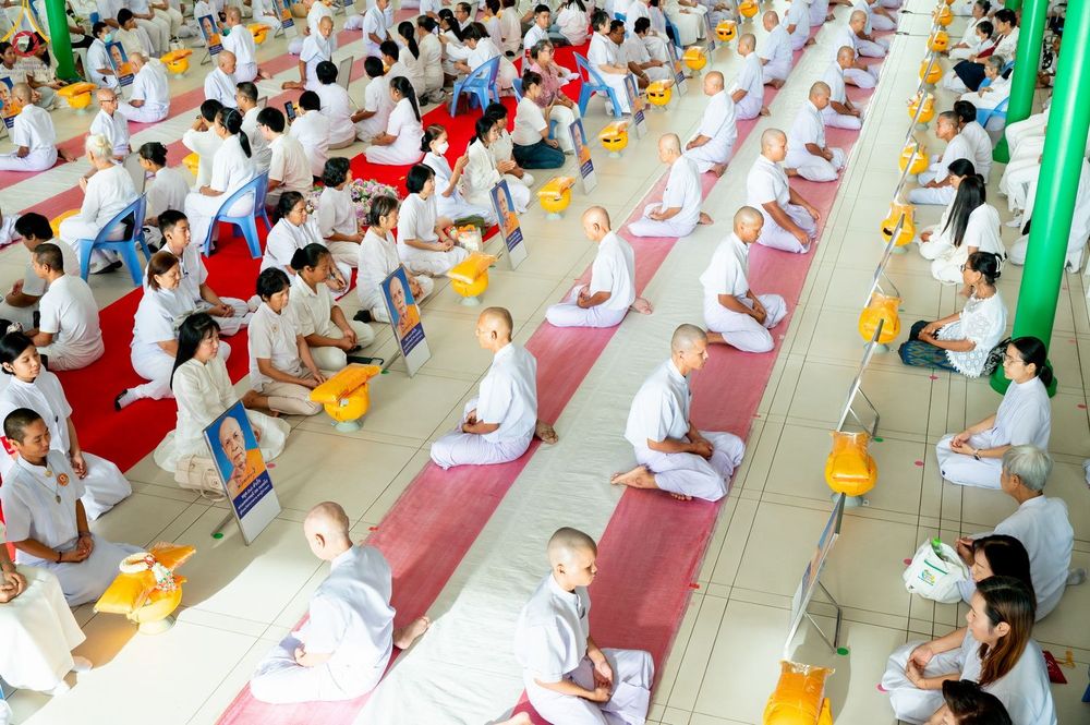 กลุ่มคนสวมชุดขาวนั่งสมาธิเรียงแถวภายในโบสถ์พระไตรปิฎกเพื่อเข้าร่วมพิธีบรรพชาอุปสมบท