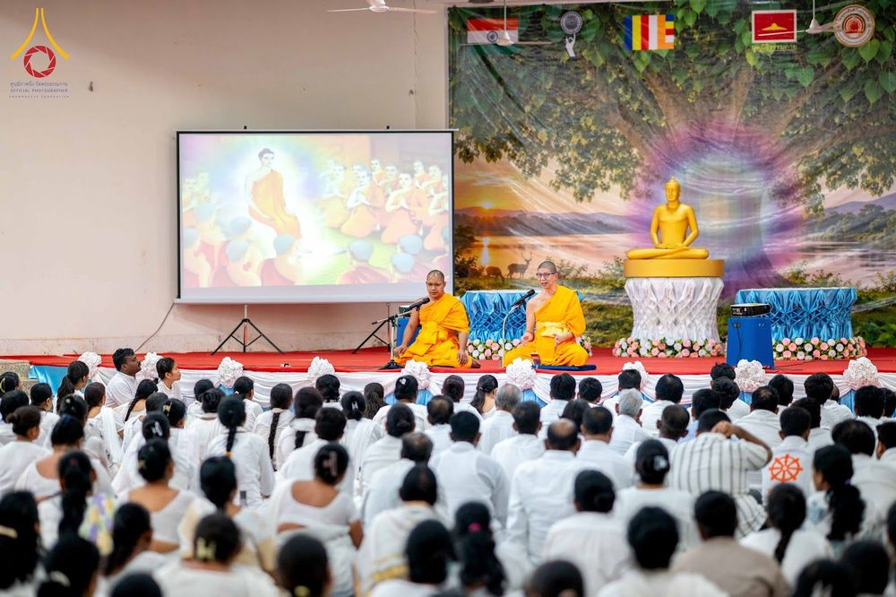 พระภิกษุสงฆ์กำลังบรรยายธรรมให้แก่ผู้ปฏิบัติธรรมที่สวมชุดขาวจำนวนมากภายในอาคาร