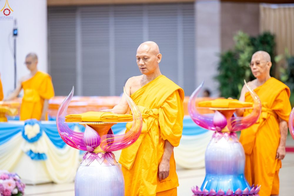 พระภิกษุสงฆ์กำลังประกอบพิธีทอดผ้าป่าโดยวางมือบนผ้าไตรที่วางอยู่บนพานพุ่มดอกบัว