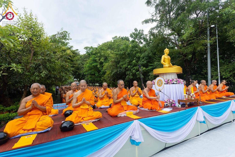 พระสงฆ์และสามเณรนั่งพนมมือบนเวทีในพิธีตักบาตรกลางแจ้ง
