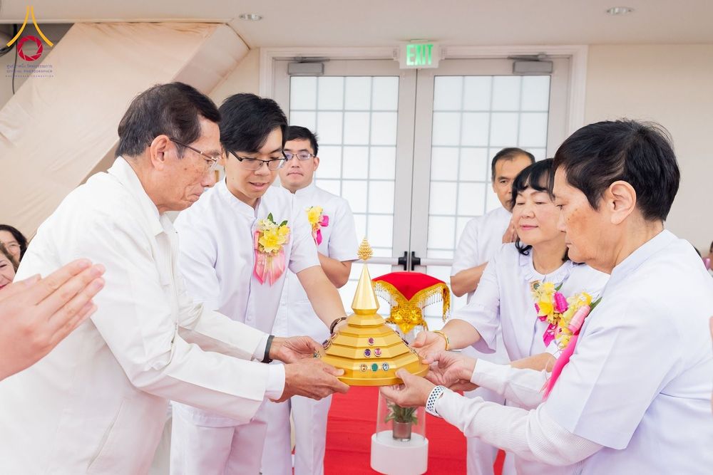 กลุ่มคนในชุดสีขาวกำลังประคองพานทองที่มีผอบทรงเจดีย์สีทองในพิธีทางศาสนา