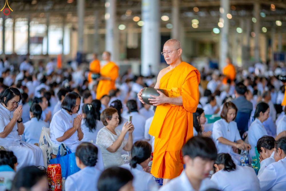 พระภิกษุสงฆ์เดินรับบิณฑบาตท่ามกลางพุทธศาสนิกชนชุดขาวในอาคารกว้าง