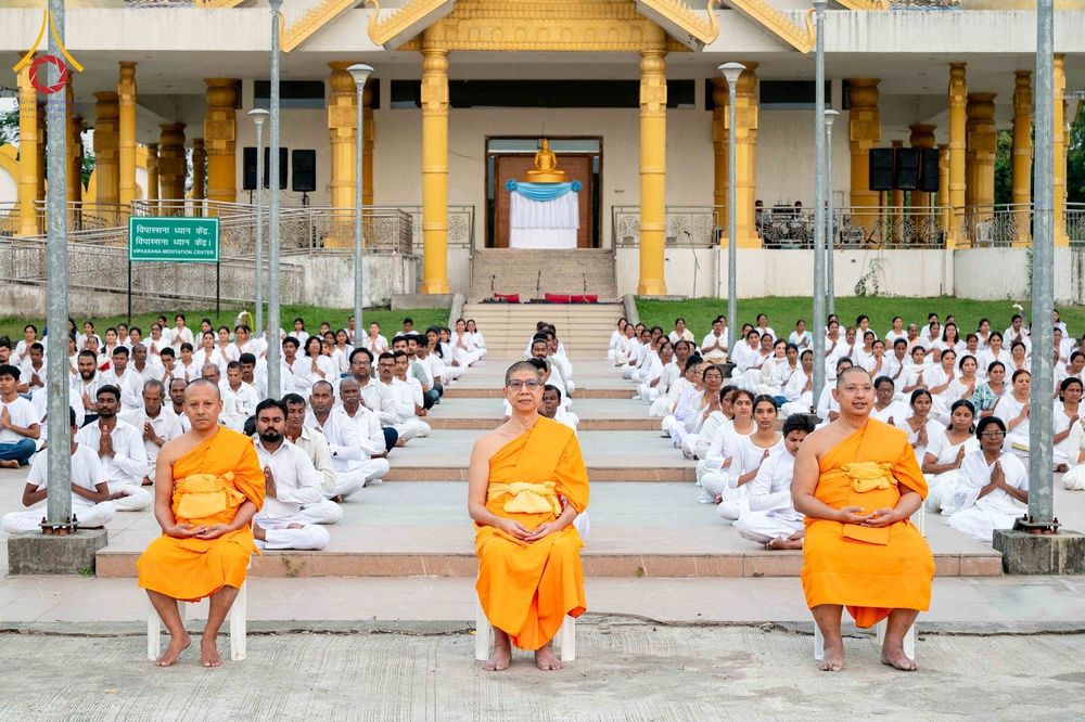 พระสงฆ์และกลุ่มผู้ปฏิบัติธรรมชุดขาวนั่งทำสมาธิหน้าอาคารพุทธสถาน