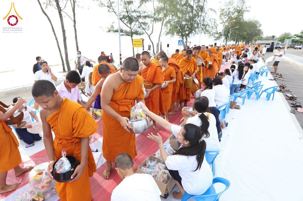 พระภิกษุสามเณรเดินรับบิณฑบาตจากประชาชนที่นั่งรอใส่บาตรริมชายหาด