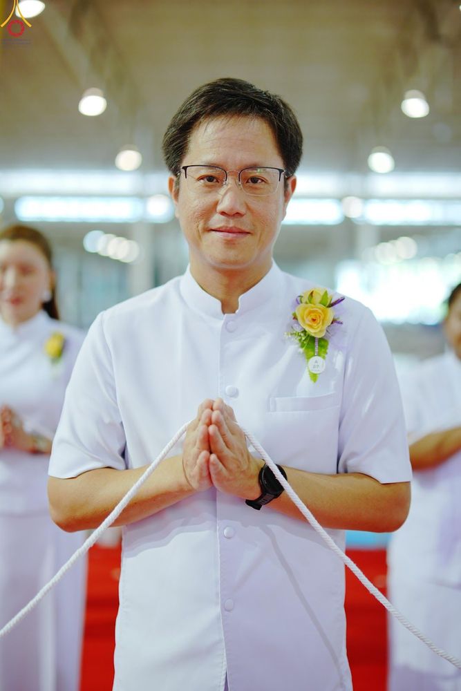 ชายสวมชุดขาวประนมมือถือสายสิญจน์ในพิธีทางศาสนา
