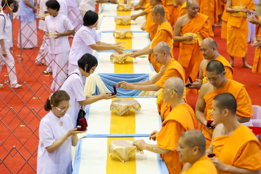 พระภิกษุสงฆ์และพุทธศาสนิกชนชุดขาวกำลังทำพิธีมอบและรับพระของขวัญในห้องโถง