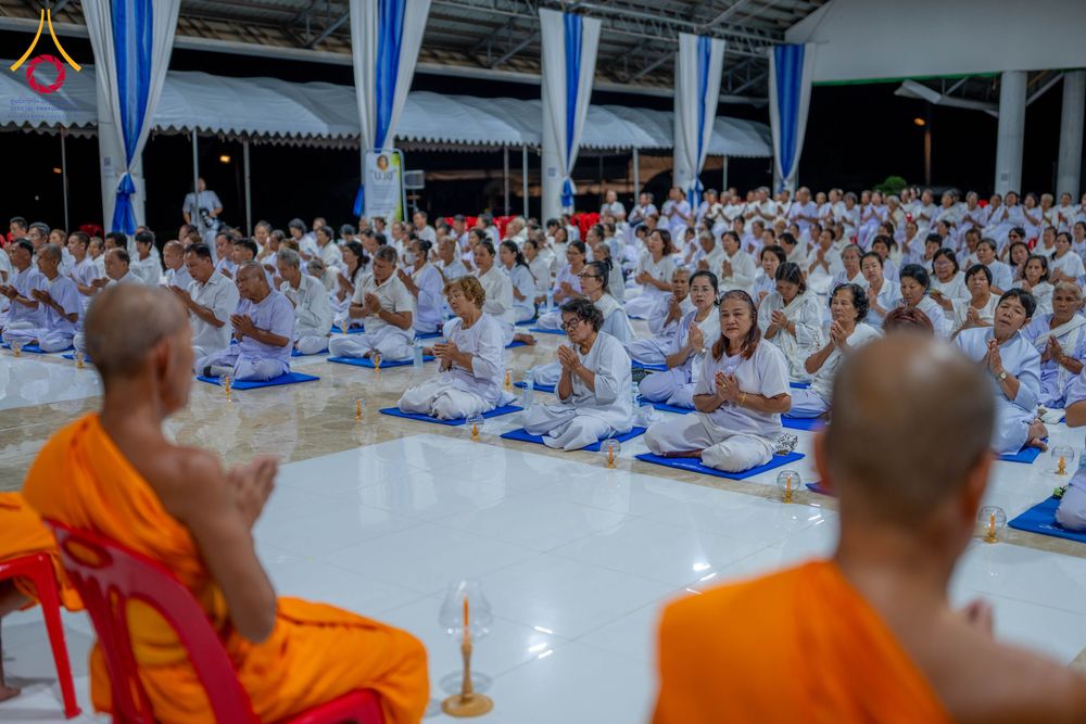 กลุ่มคนสวมชุดขาวนั่งพนมมือปฏิบัติธรรมต่อหน้าพระภิกษุสงฆ์ภายในอาคาร