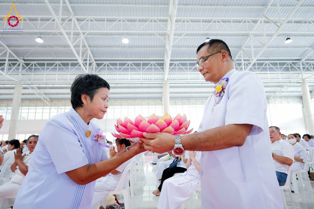 ชายและหญิงสวมชุดสีขาวกำลังประคองพานดอกบัวสีชมพูร่วมกันในพิธีทางศาสนา