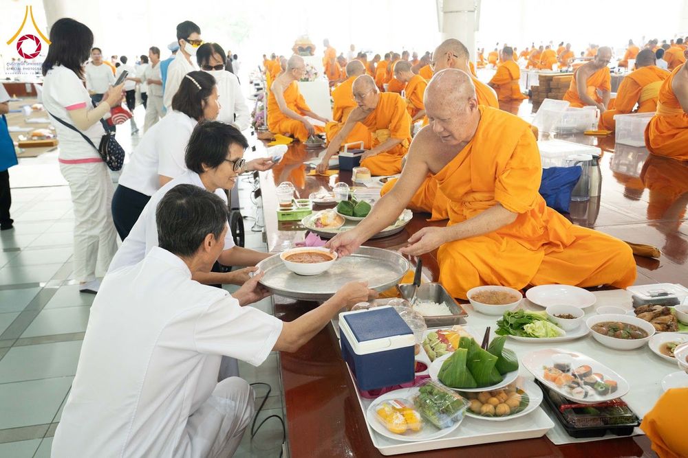 พุทธศาสนิกชนชุดขาวกำลังประเคนอาหารใส่ถาดให้พระภิกษุสงฆ์ในหอฉัน
