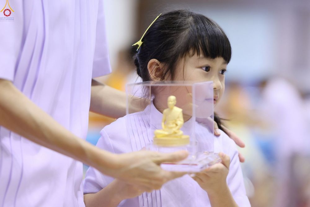 เด็กหญิงสวมชุดขาวถือกล่องใสบรรจุพระพุทธรูปองค์เล็กในงานพิธี