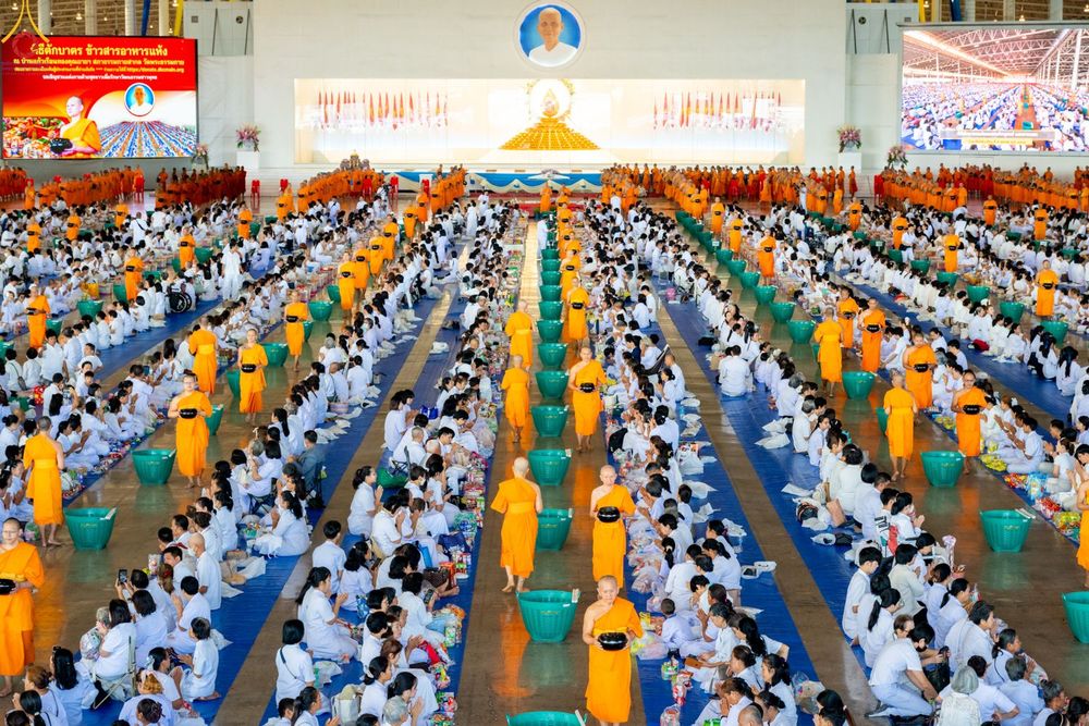 พุทธศาสนิกชนชุดขาวจำนวนมากนั่งเรียงแถวภายในสภาธรรมกายสากลเพื่อร่วมพิธีตักบาตรข้าวสารอาหารแห้งแด่พระภิกษุสงฆ์