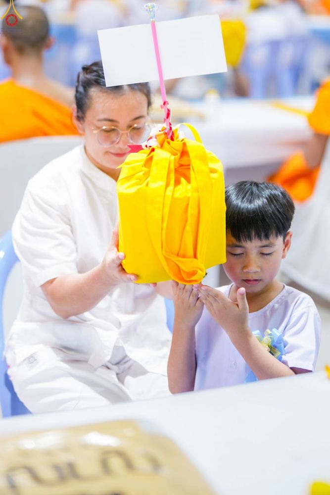 หญิงสาวและเด็กชายสวมชุดขาวกำลังประคองถุงสังฆทานสีเหลืองเพื่อเตรียมถวายพระสงฆ์
