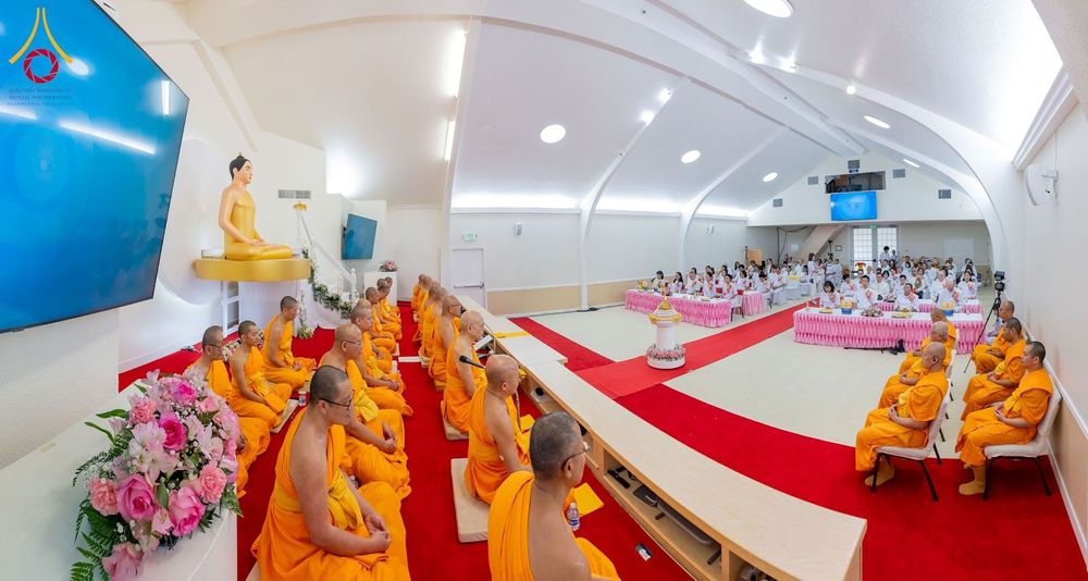 พระภิกษุสงฆ์และพุทธศาสนิกชนกำลังร่วมพิธีกรรมทางศาสนาภายในอาคารที่มีพระพุทธรูปประดิษฐานอยู่