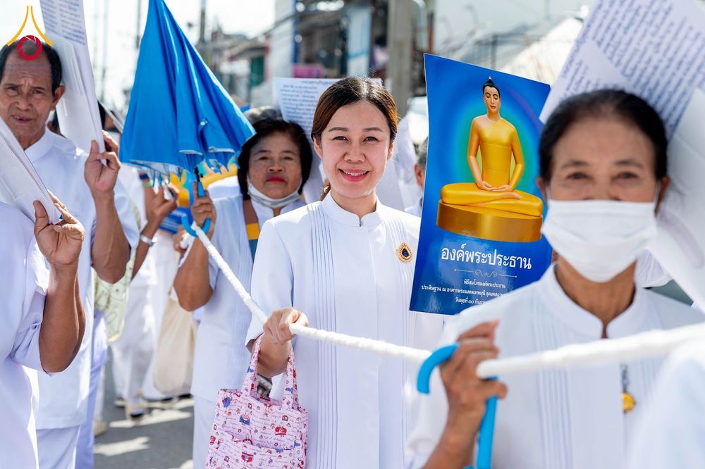 กลุ่มคนสวมชุดขาวถือป้ายภาพพระพุทธรูปและเชือกในขบวนพิธีทางศาสนา