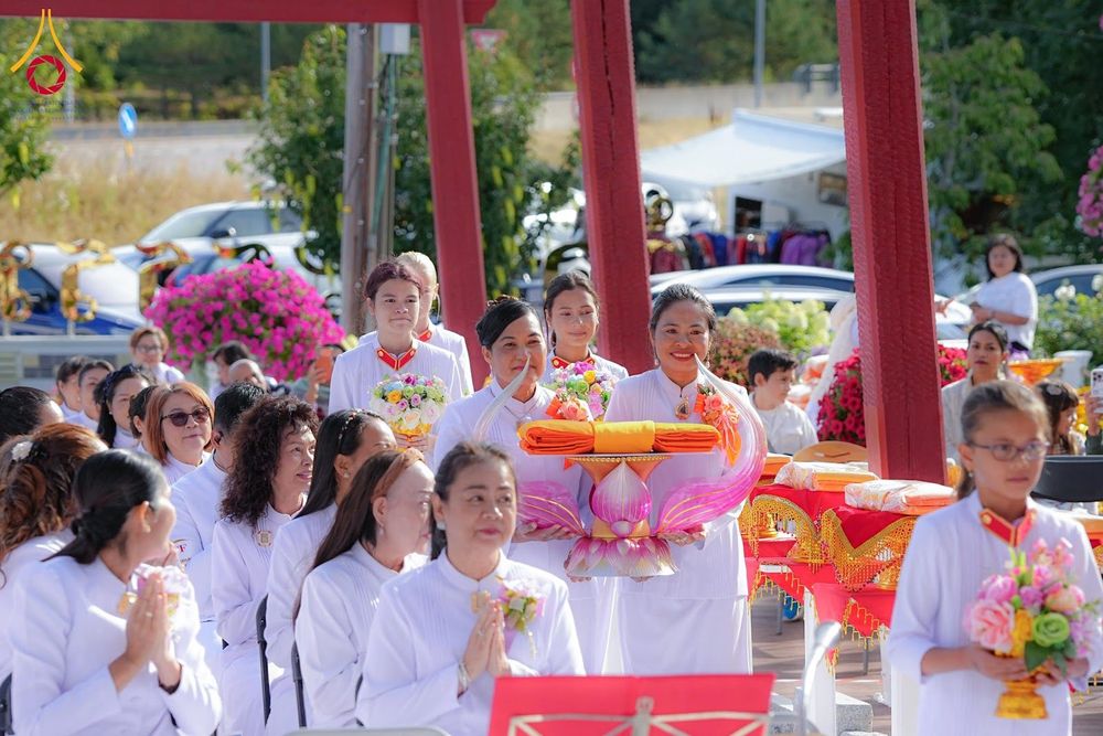 กลุ่มคนสวมชุดสีขาวถือพานพุ่มผ้าไตรจีวรในพิธีทางศาสนาพุทธ