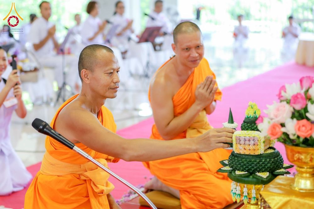 พระสงฆ์สองรูปกำลังประกอบพิธีกรรมทางศาสนาและประพรมน้ำพระพุทธมนต์ลงบนพานพุ่มดอกไม้