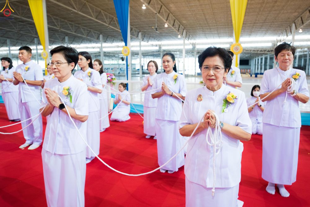 กลุ่มคนสวมชุดขาวถือสายสิญจน์และพนมมือร่วมพิธีทางศาสนา