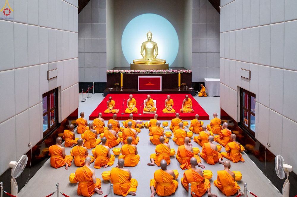 กลุ่มพระภิกษุและสามเณรนั่งสมาธิภายในโบสถ์ที่มีพระพุทธรูปสีทองเป็นประธาน