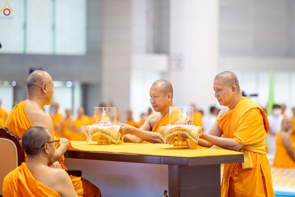 พระภิกษุสงฆ์กำลังทำพิธีมอบพระของขวัญที่บรรจุในครอบแก้วใสบนพานทองภายในห้องโถง
