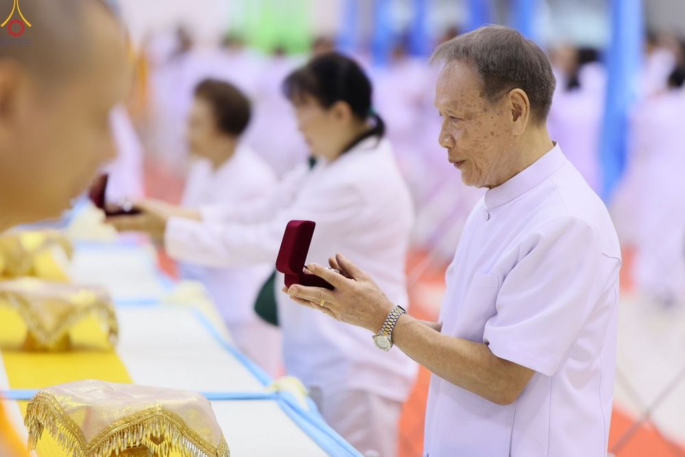 ชายสูงวัยสวมชุดสีขาวถือกล่องพระของขวัญสีแดงในพิธีการ