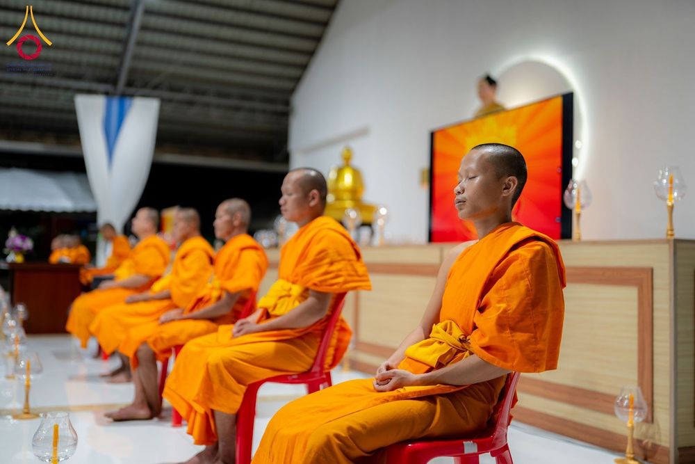 พระภิกษุสงฆ์หลายรูปนั่งสมาธิเรียงแถวกันภายในอาคารปฏิบัติธรรม