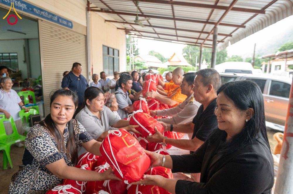 กลุ่มคนและพระภิกษุกำลังส่งมอบถุงยังชีพสีแดงให้แก่ประชาชนในพื้นที่ประสบภัย