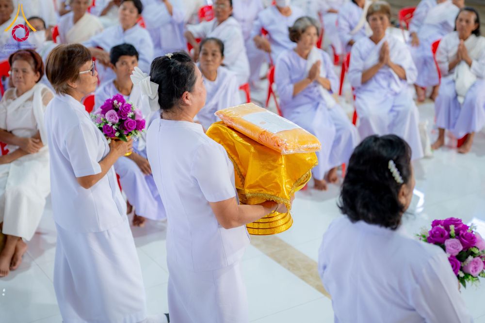 กลุ่มผู้หญิงในชุดสีขาวกำลังถือพานพุ่มผ้าไตรและช่อดอกไม้ในพิธีทางศาสนา