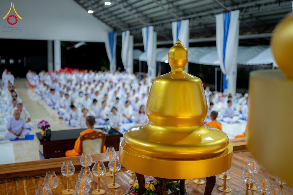 พระพุทธรูปสีทองตั้งอยู่หน้ากลุ่มผู้เข้าร่วมโครงการอบรมในชุดสีขาวภายในอาคาร
