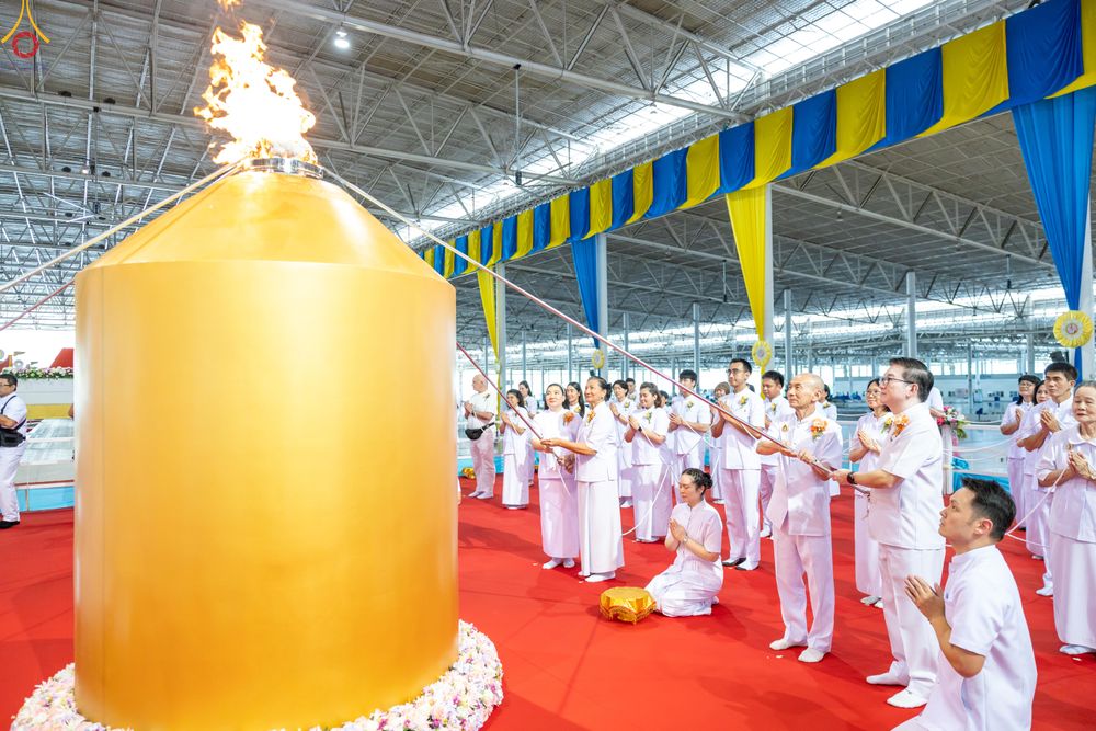 กลุ่มคนในชุดขาวกำลังประกอบพิธีจุดเทียนใจ ไฟนิรันดร์ อนันตชัย โดยมีโคมไฟสีทองขนาดใหญ่อยู่ด้านหน้า