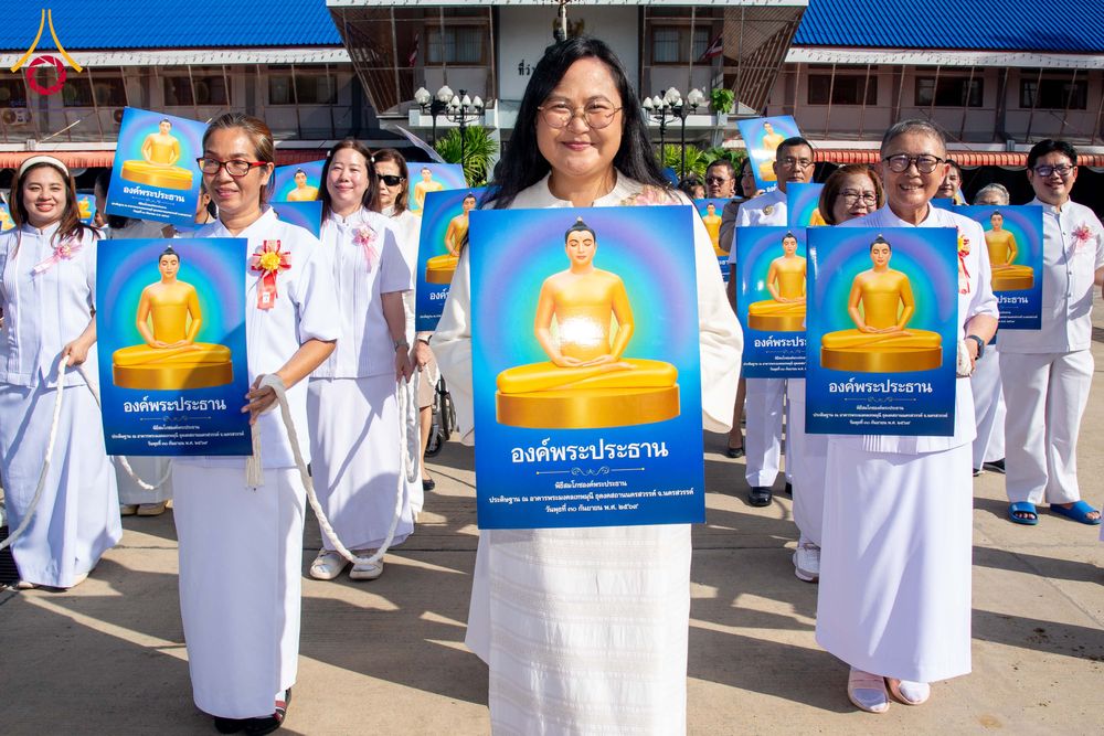 กลุ่มคนสวมชุดขาวถือป้ายภาพพระพุทธรูปสีทองในพิธีทางศาสนา