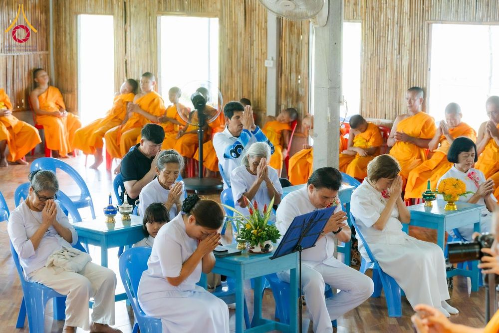 กลุ่มพุทธศาสนิกชนและพระภิกษุสงฆ์กำลังพนมมือประกอบพิธีทางศาสนาภายในอาคาร
