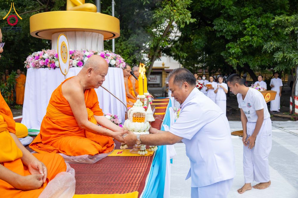 ชายสวมชุดขาวกำลังถวายสิ่งของแด่พระภิกษุสงฆ์ในพิธีตักบาตรสามเณรธรรมทายาท