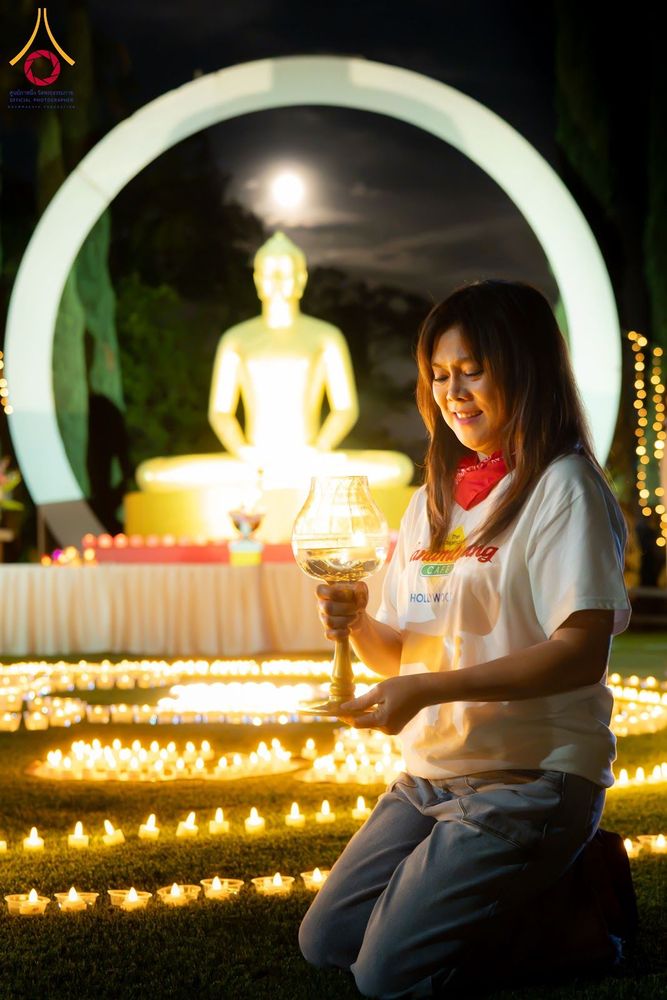 หญิงสาวถือโคมประทีปท่ามกลางแสงเทียนจำนวนมากในยามค่ำคืน โดยมีพระพุทธรูปเป็นฉากหลัง