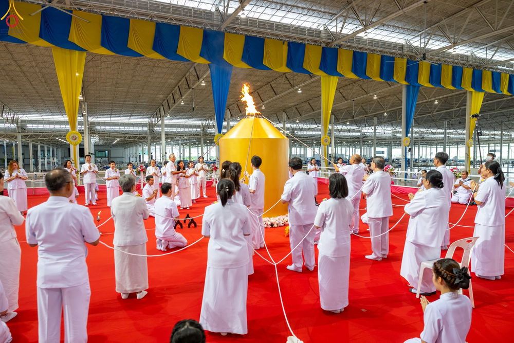 กลุ่มคนในชุดขาวกำลังร่วมพิธีจุดเทียนใจ ไฟนิรันดร์ อนันตชัย โดยมีโคมไฟสีทองตั้งอยู่ตรงกลางและมีสายสิญจน์เชื่อมโยงถึงผู้เข้าร่วมพิธี
