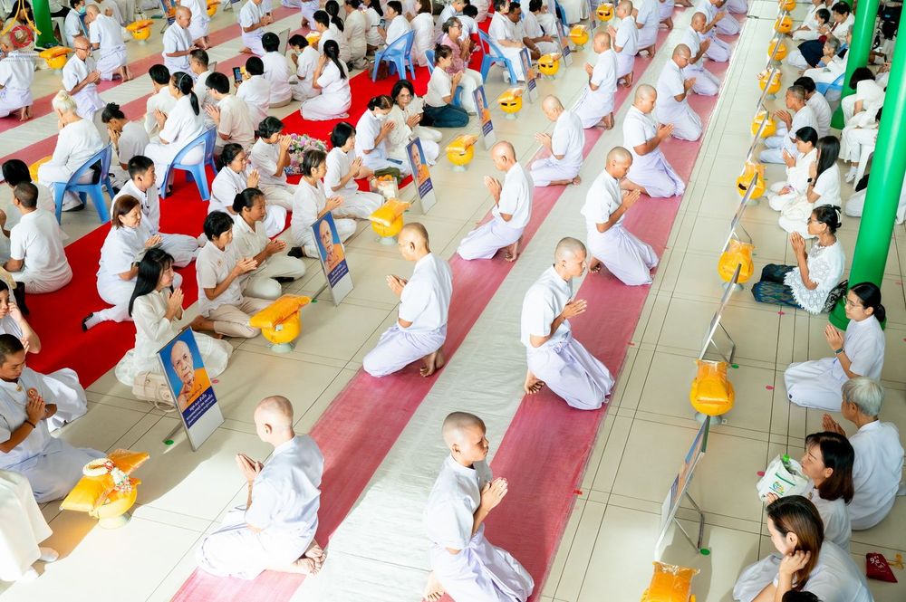 กลุ่มผู้เข้าร่วมพิธีบรรพชาอุปสมบทหมู่ในชุดขาวนั่งพนมมือเรียงแถวอย่างเป็นระเบียบภายในอาคาร