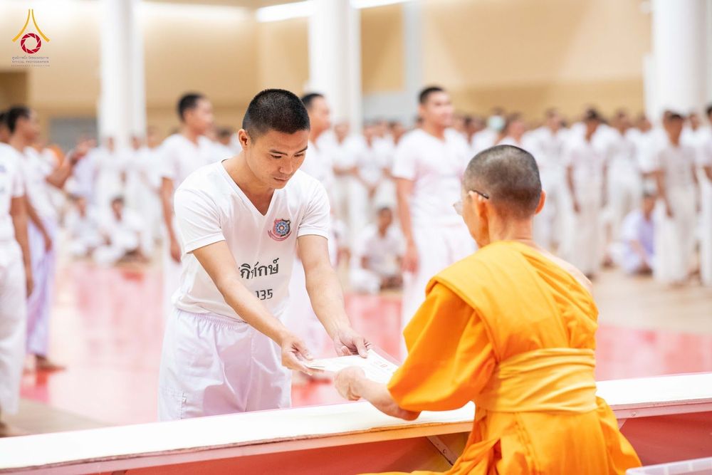 นักเรียนนายสิบตำรวจสวมชุดขาวกำลังรับเกียรติบัตรจากพระภิกษุสงฆ์ในพิธีปิดโครงการบรรพชา