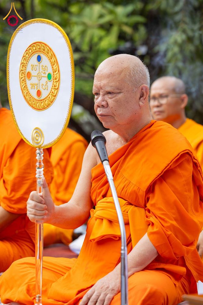 พระภิกษุสงฆ์ถือตาลปัตรและมีไมโครโฟนตั้งอยู่ด้านหน้าในพิธีทางศาสนา