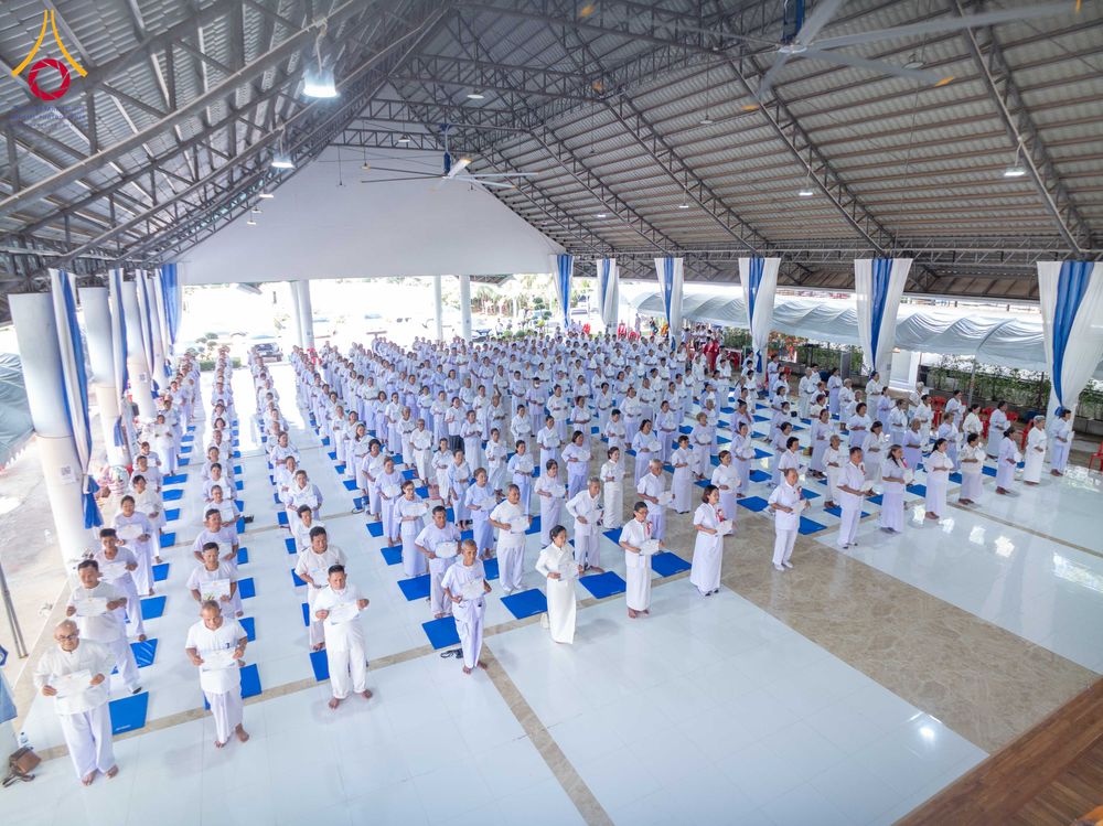 กลุ่มผู้เข้าร่วมโครงการอบรมสวมชุดขาวจำนวนมากยืนเรียงแถวอย่างเป็นระเบียบภายในอาคารปฏิบัติธรรม