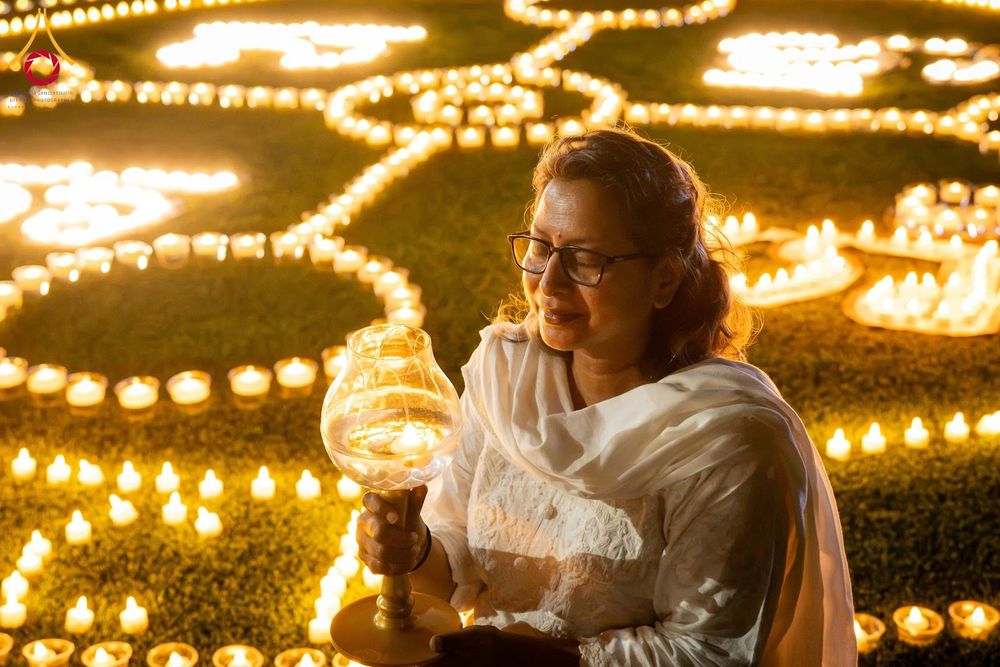 หญิงสวมชุดสีขาวถือโคมประทีปท่ามกลางการจุดประทีปจำนวนมากบนพื้นหญ้าในยามค่ำคืน